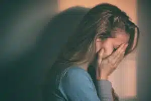 Woman overwhelmed by heroin addiction with face in hands seeking